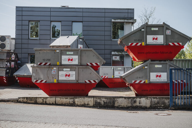 Stapel aus beschrifteten Muldencontainern vor Firmengebäude in Hamburg – zuverlässiger Containerdienst für Wertstoffsammlung