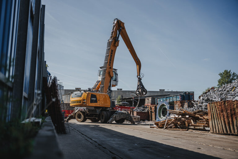 Alt-Text: Bagger mit Greifarm beim Bewegen von Metallschrott auf dem Recyclinghof eines Entsorgungsfachbetriebs in Hamburg